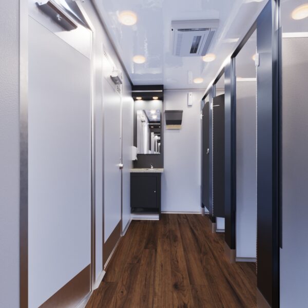 A spacious corridor view inside a luxury restroom trailer showing multiple stalls and modern amenities.