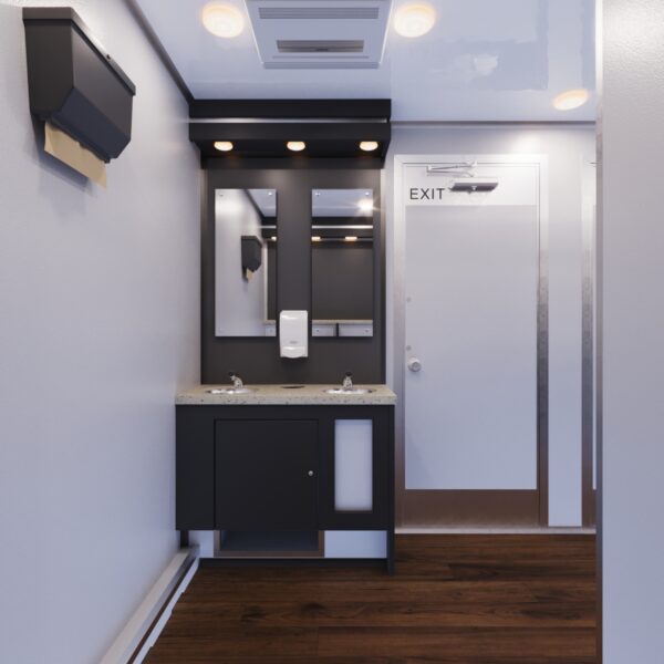 Corner view inside a luxury restroom trailer highlighting a sink, mirror, and well-lit vanity area.